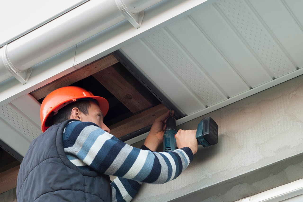 Installer fitting ventilated white uPVC soffits beneath a roofline